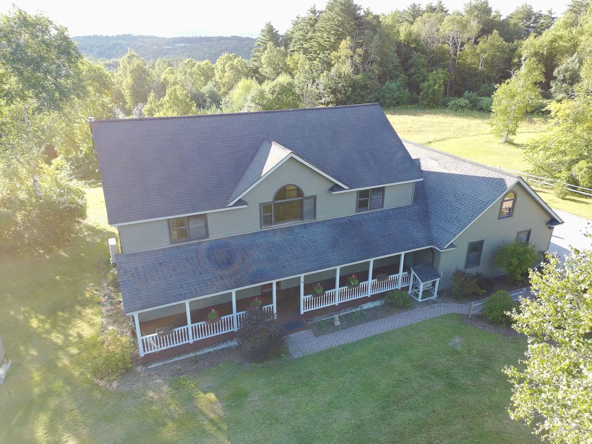 Aerial view of a home's rear yard, deck, and tree line